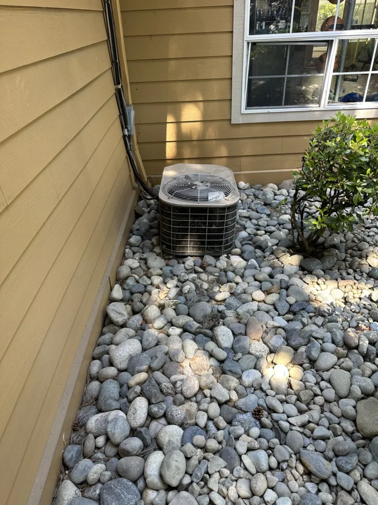 Heat pump condenser set in a river-rock bed beside a building