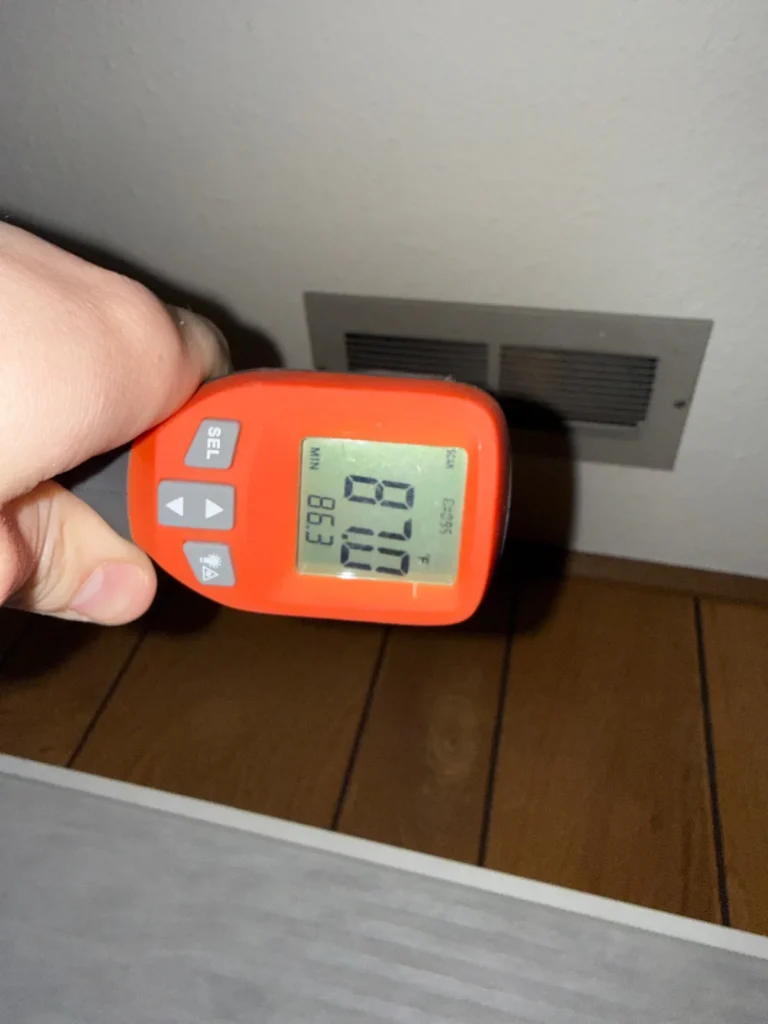 Technician checking supply air temperature at a register