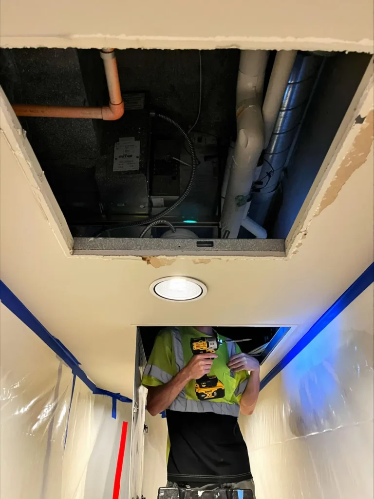 Omni Mechanical technician working on a fan coil through a ceiling opening