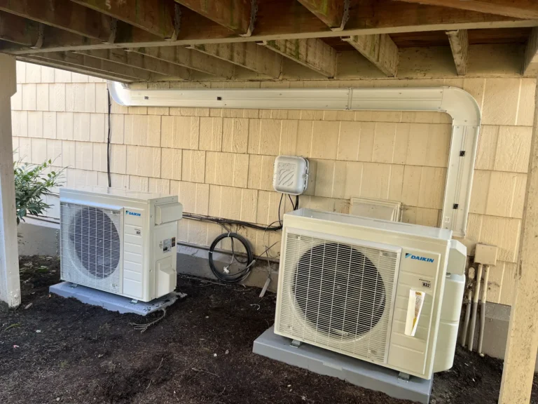 Two Daikin heat pump condensers with white line-set covers under a deck in Redmond